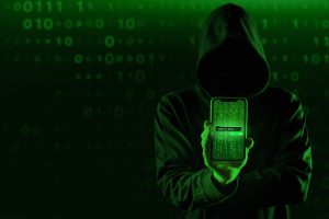 “Kapüşonlu karanlık bir kişi, elindeki cep telefonuyla dijital dolandırıcılık suçu ve siber suçları simgeliyor – mobil siber saldırı ve hacker temalı görsel”