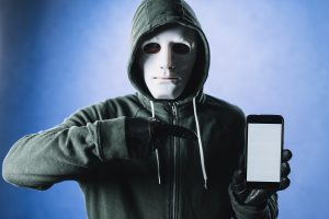 “Kapüşonlu sweatshirt ve beyaz maske takan kişi, elinde telefon tutuyor – sosyal medyada anonim hesaplar ve dijital suçları temsil eden görsel”