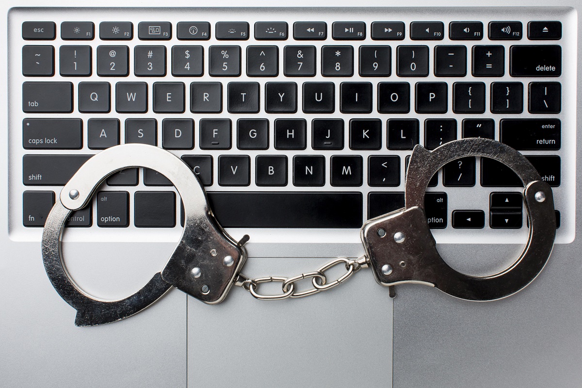 “Laptop klavyesi üzerinde duran kelepçe – sosyal medyada hakaret suçunu simgeleyen adli temalı görsel”